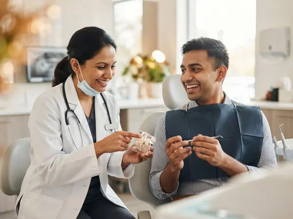 The dentist explaining a treatment to a smiling patient with a dental model